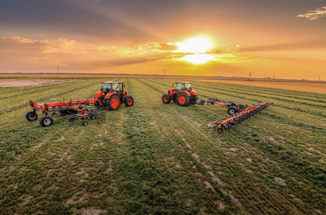Tractors working in the field with hay tools during sunset