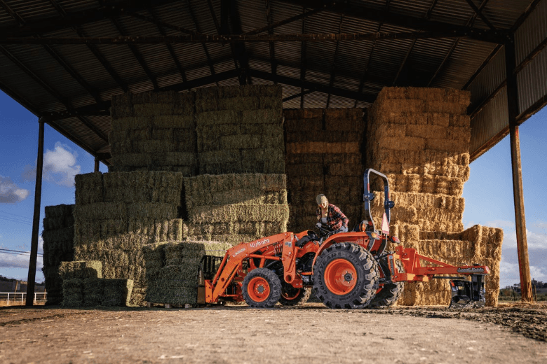 Woman using tractor to lift a large load of hay stacks
