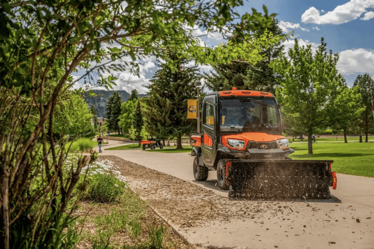 RTV using a front sweeper attachment at the grounds of a school