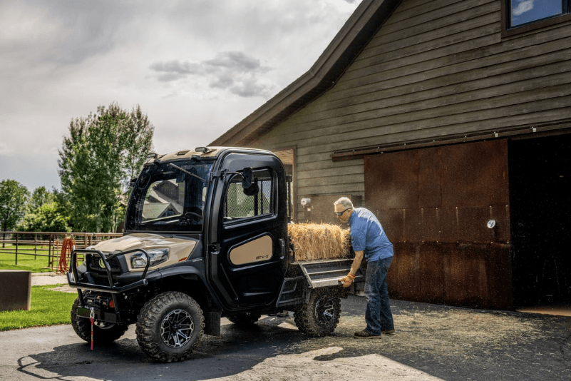 Man unloading hay stack from cargo bed of RTV