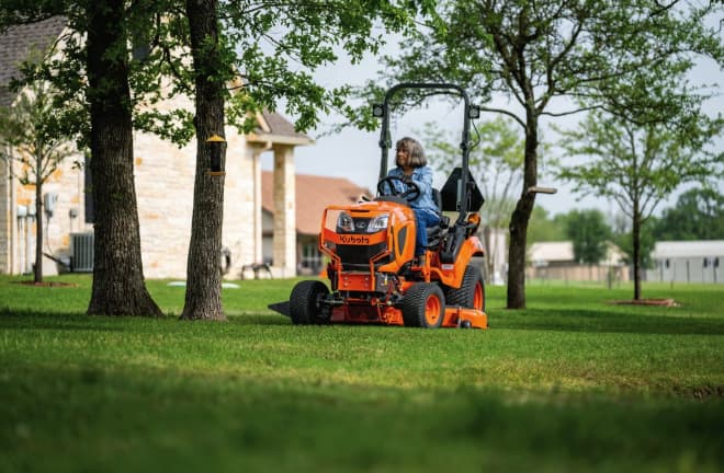 Woman driving a Kubota BX Series sub-compact tractor with mower deck in a residential yard