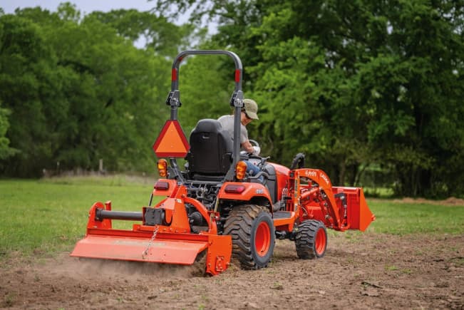 Kubota BX2380 tractor with rear tiller attachment cultivating soil in an open field