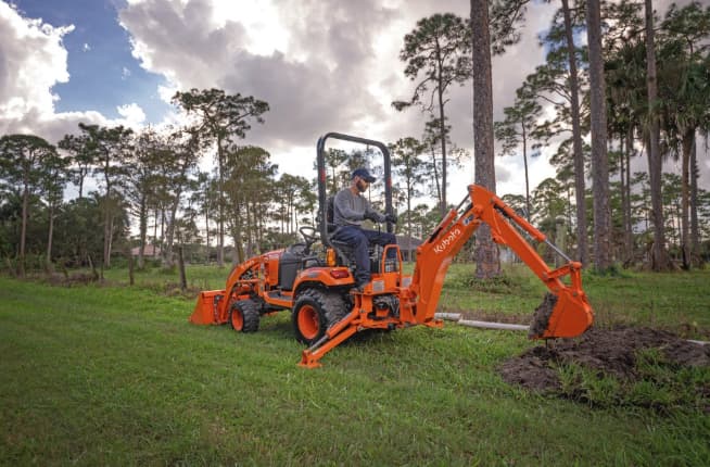 Kubota BX23S tractor with backhoe attachment digging a trench in a grassy lot